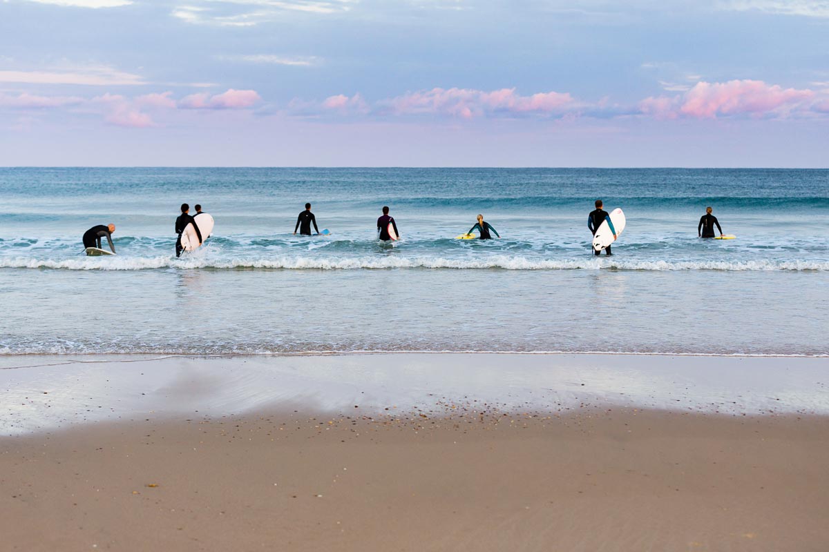 Surfschüler warten mit ihren Boards im Wasser auf die nächste Welle