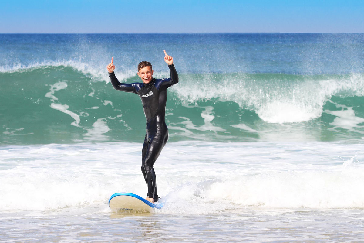 Surfer steht jubelnd auf seinem Softboard nach einem erfolgreichen Take-off